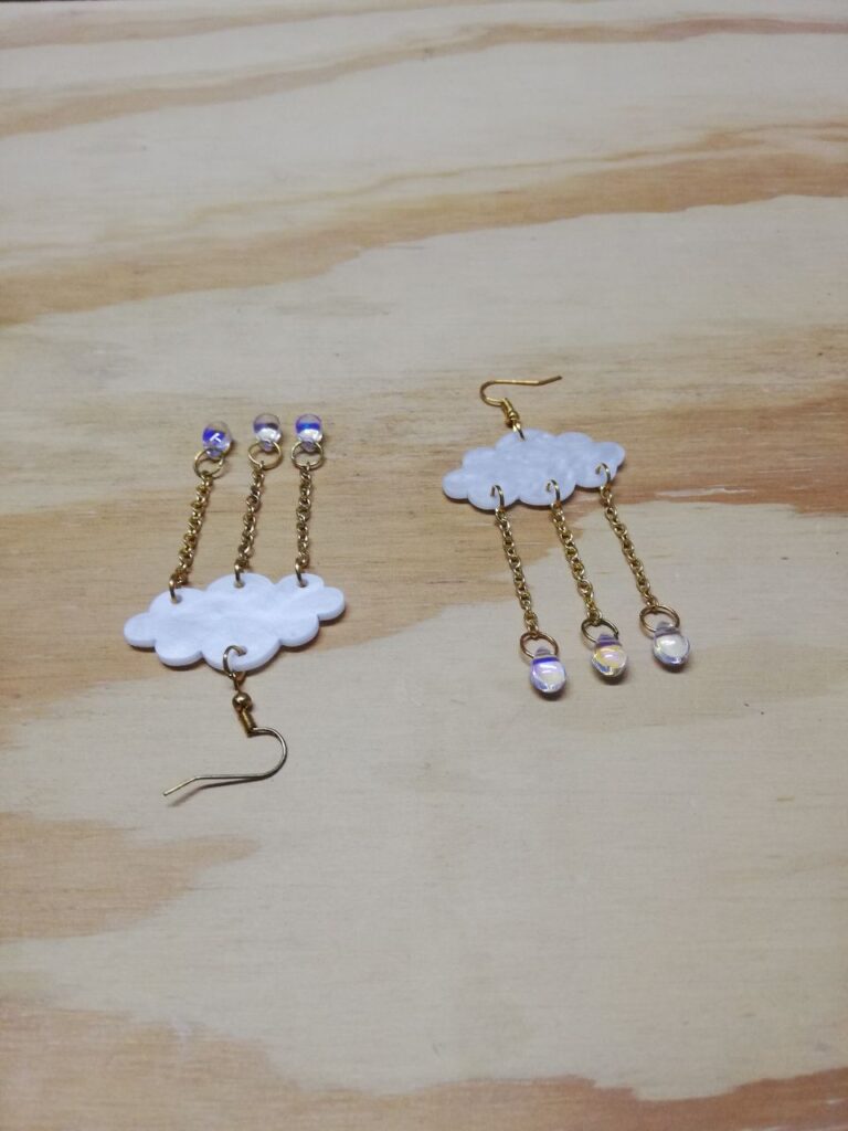 Fotografía de aretes Lluvia Iridiscente encontrados. Precio: $50 MXN Dimensiones de dije: 6.5 centímetros Material: Metal, acrílico y plástico Color de materiales: Dorado, blanco nacarado y transparente iridiscente Tipo de agarre: Gancho Categoría: Nuevo