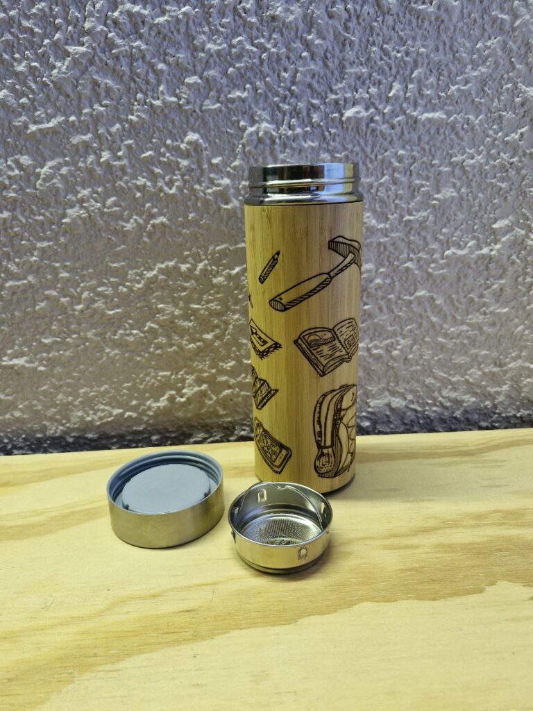 Fotografía de termo Ciencias de la Tierra con la tapa e infusionador a un costado. Precio: $600 MXN Marca: Dino Tools Dimensiones: Ancho 7 cm., Alto 20.6 cm. Capacidad: 500 ml. Color: Madera clara Materiales: Acero SUS 304, bambú y plástico Categoría: Nuevo