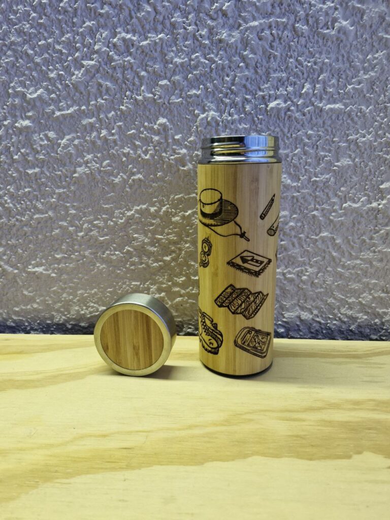 Fotografía de termo Ciencias de la Tierra con la tapa a un costado. Precio: $600 MXN Marca: Dino Tools Dimensiones: Ancho 7 cm., Alto 20.6 cm. Capacidad: 500 ml. Color: Madera clara Materiales: Acero SUS 304, bambú y plástico Categoría: Nuevo