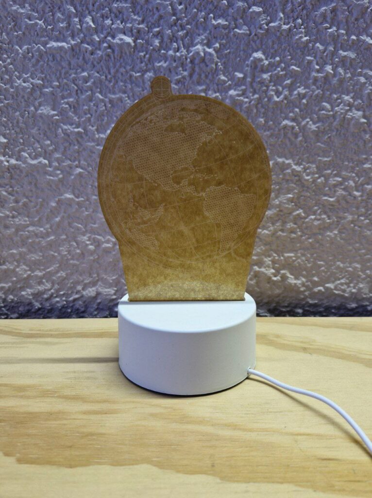 Fotografía de frente de lámpara de acrílico de globo terráqueo apagada en un entorno iluminado Precio: $125 MXN Materiales: Plástico, acrílico Medidas: Base: Ancho 9.5 cm. y Alto 4 cm.; Altura total: 19.5 cm.; Largo cable: 83 cm. Color de base: Blanco Color de acrílico: Transparente Tipo de alimentación: USB Luz: Cálida Categoría: Nuevo