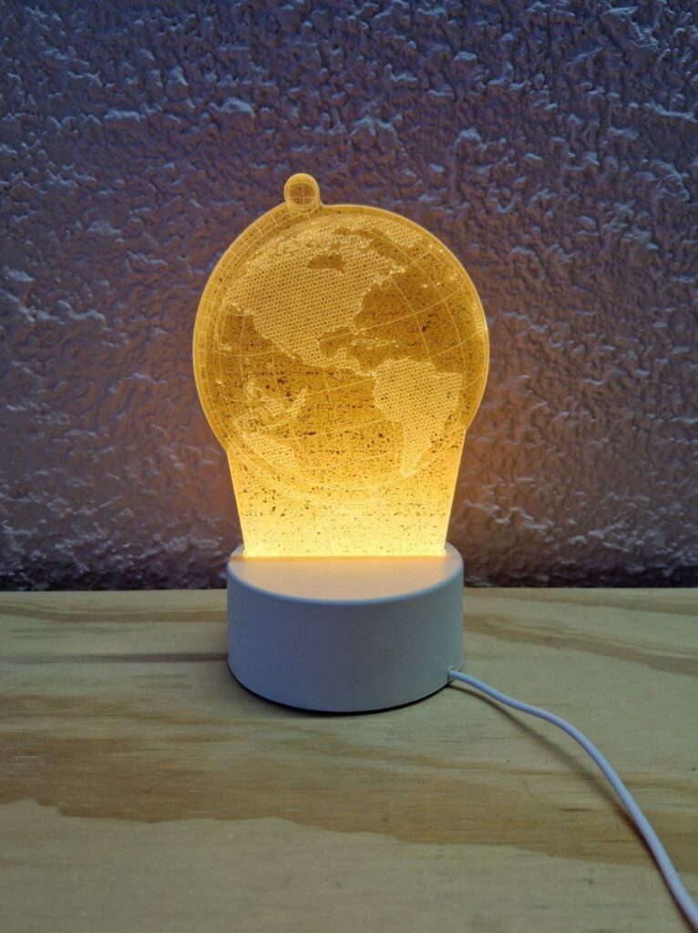 Fotografía de frente de lámpara de acrílico de globo terráqueo prendida en un entorno iluminado Precio: $125 MXN Materiales: Plástico, acrílico Medidas: Base: Ancho 9.5 cm. y Alto 4 cm.; Altura total: 19.5 cm.; Largo cable: 83 cm. Color de base: Blanco Color de acrílico: Transparente Tipo de alimentación: USB Luz: Cálida Categoría: Nuevo