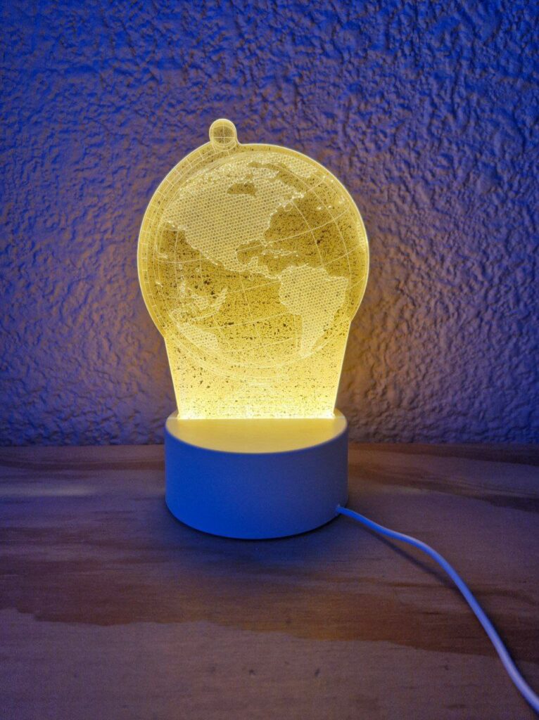 Fotografía de frente de lámpara de acrílico de globo terráqueo prendida en un entorno oscuro Precio: $125 MXN Materiales: Plástico, acrílico Medidas: Base: Ancho 9.5 cm. y Alto 4 cm.; Altura total: 19.5 cm.; Largo cable: 83 cm. Color de base: Blanco Color de acrílico: Transparente Tipo de alimentación: USB Luz: Cálida Categoría: Nuevo