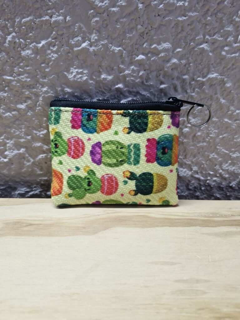 Fotografía de frente de monedero Cactus. Precio: $20 MXN Dimensiones: 11 x 9 centímetros Material: Yute plástico Color de base: Blanco Tipo de cierre: Plástico con carrito metálico Forro: Negro Categoría: Nuevo