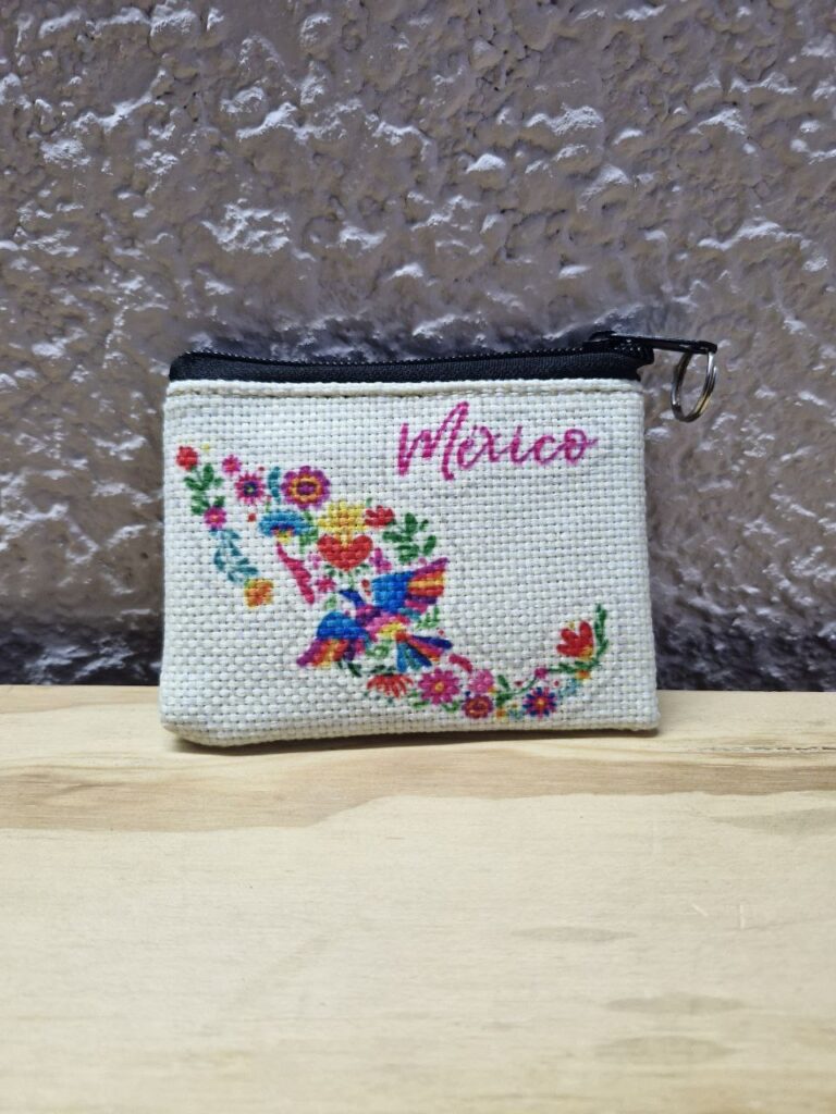 Fotografía de frente de monedero México Floral. Precio: $20 MXN Dimensiones: 11 x 9 centímetros Material: Yute plástico Color de base: Blanco Tipo de cierre: Plástico con carrito metálico Forro: Negro Categoría: Nuevo
