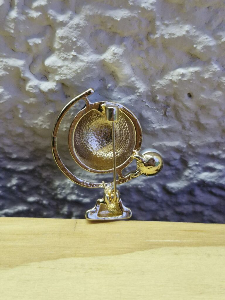 Fotografía de detrás de broche Globo Terráqueo y Luna. Precio: $100 MXN. Dimensiones aproximadas: Ancho 3 cm. x Alto 3.6 cm. x Grueso 1.8 cm Material: Metal y plástico. Colores: Dorado, azul y aperlado. Categoría: Nuevo.