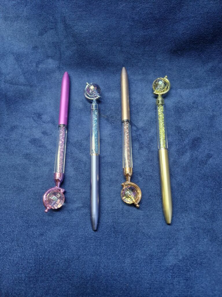 Fotografía de cuatro lapiceros globo terráqueo brillantes en color rosa mexicano, celeste, oro rosado y dorado. Precio: $25 MXN c/u Dimensiones: Largo: 17 cm., Ancho: 1 cm. Material: Plástico Colores de cuerpo: Rosa, Palo de rosa, Amarillo y Azul Colore de tinta: Negra Tipo de punta: Retráctil por giro
